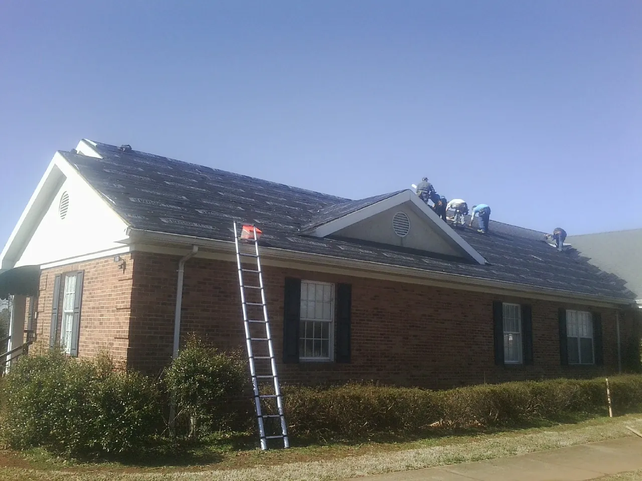 Crew tearing shingles off a brick ranch roof with a ladder set — Metal Roof Repair work by our crew in Port Reading