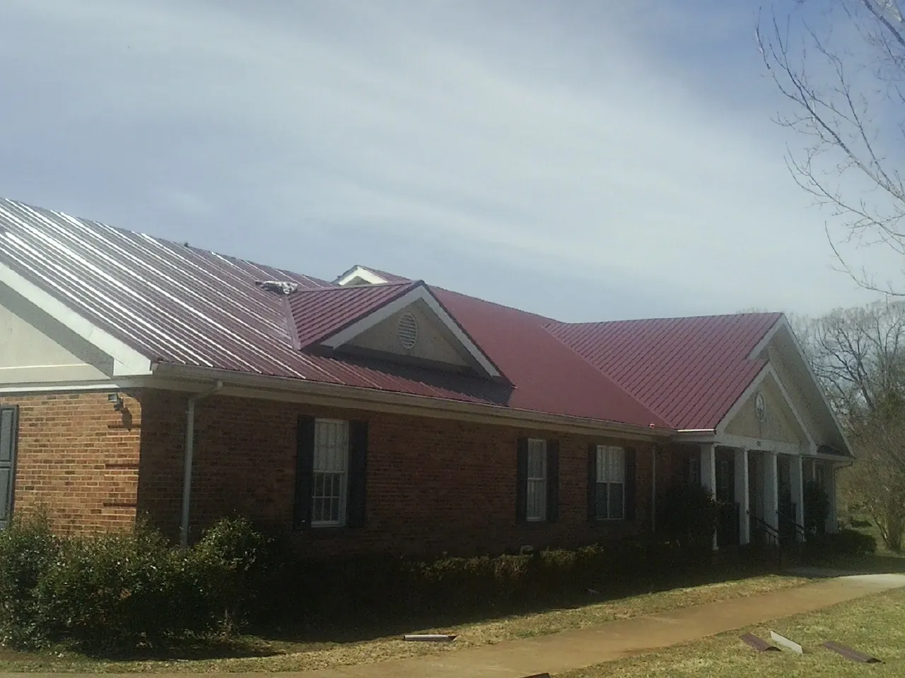 Red metal roof with gabled entries on a long brick building, from a Hail Damage Roof Repair job in Port Reading