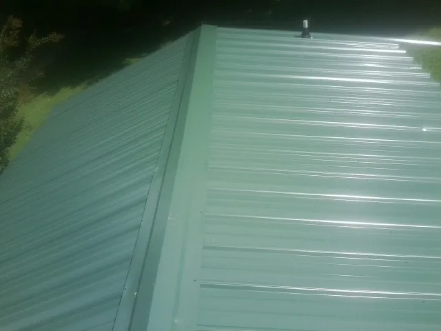 New green metal panels meeting at the ridge of a roof — Flat Roof Repair work by our crew in Port Reading