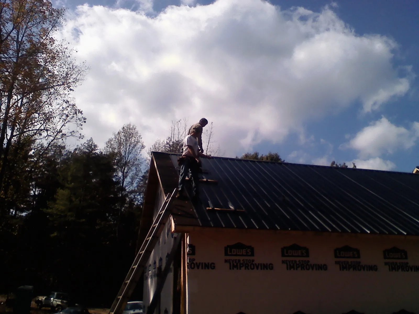 Roofer fastening dark metal panels high against a cloudy sky, from a Roof Inspection job in Port Reading