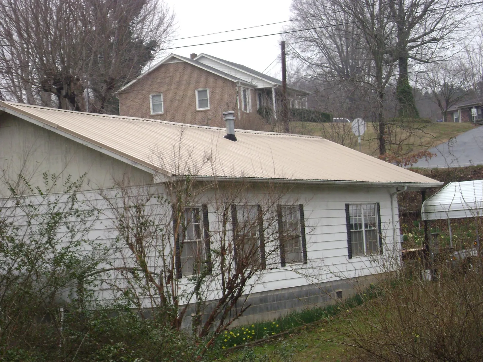 Tan metal roof on a white sided house set into a hillside — Commercial Roofing by Roofing Brothers in Port Reading