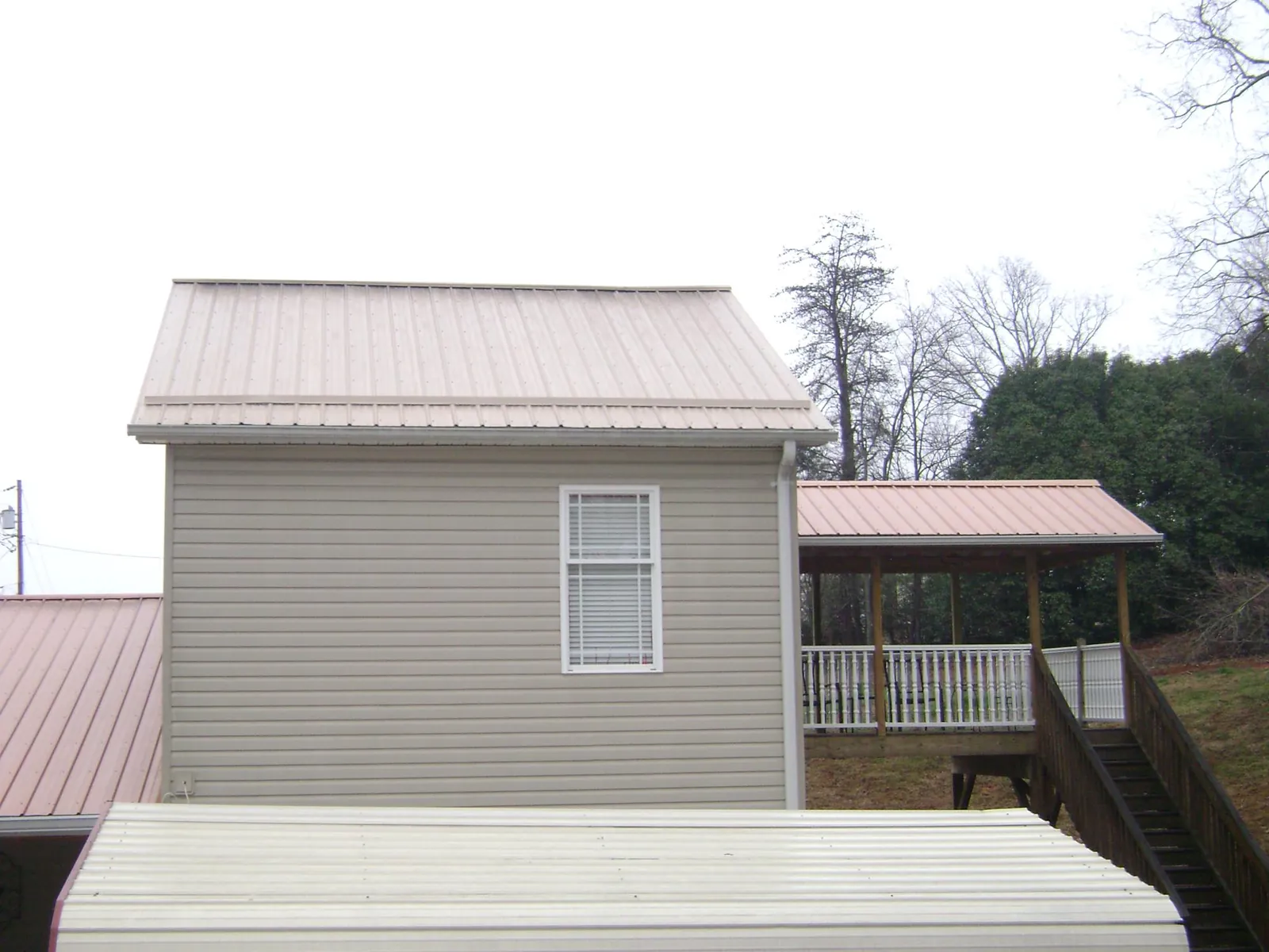 Tan metal roofs on a two story addition and attached porch, from a Roof Replacement job in Port Reading
